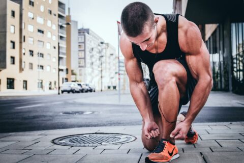 man working out outdoors, he is kneeling down tying his sneakers